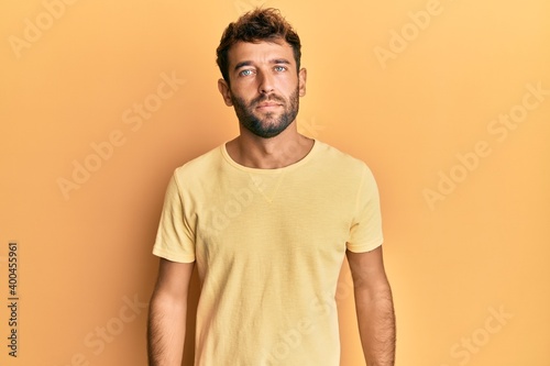 Handsome man with beard wearing casual yellow tshirt over yellow background relaxed with serious expression on face. simple and natural looking at the camera.