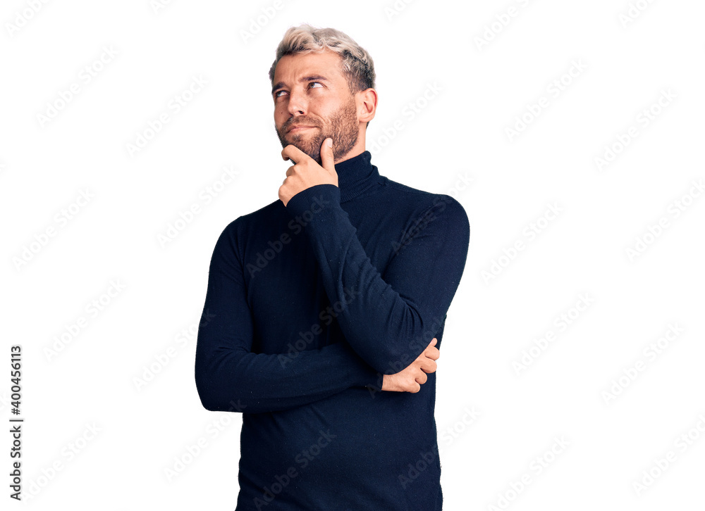Young handsome blond man wearing casual turtleneck sweater serious face thinking about question with hand on chin, thoughtful about confusing idea Young handsome blond man wearing casual turtleneck sweater serious face thinking about question with hand on chin, thoughtful about confusing idea