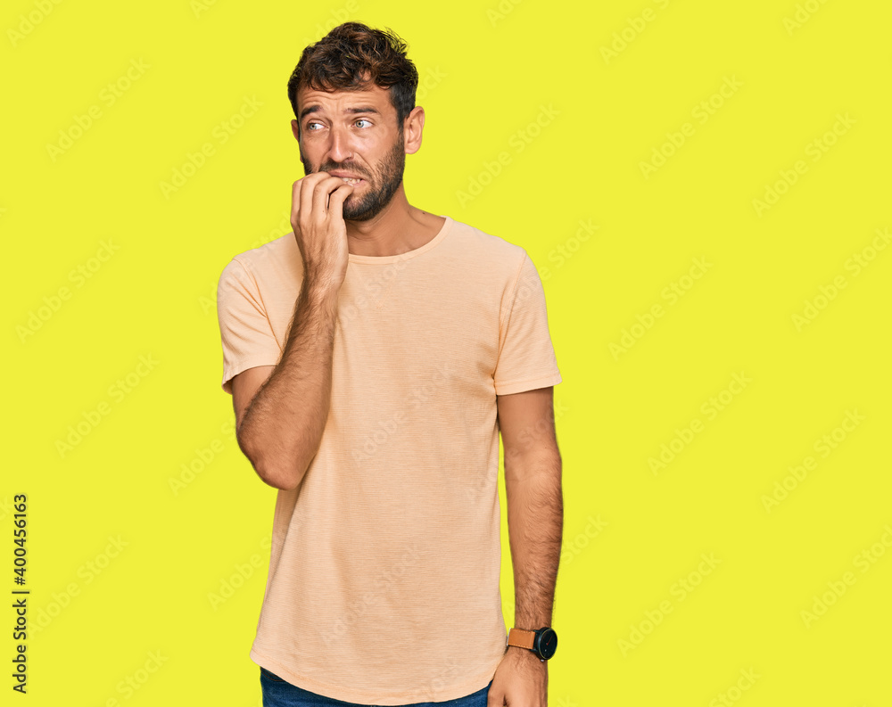 Handsome young man with beard wearing casual tshirt looking stressed and nervous with hands on mouth biting nails. anxiety problem. Handsome young man with beard wearing casual tshirt looking stressed and nervous with hands on mouth biting nails. anxiety problem.