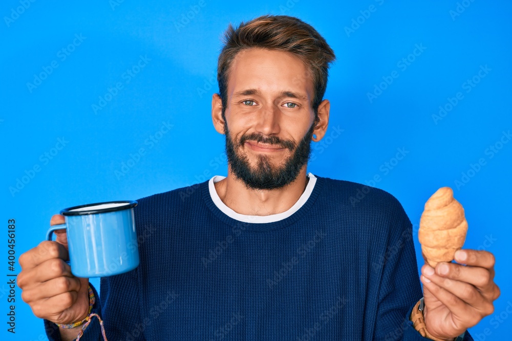 Handsome caucasian man with beard drinking a cup of coffee and croissant clueless and confused expression. doubt concept. Handsome caucasian man with beard drinking a cup of coffee and croissant clueless and confused expression. doubt concept.