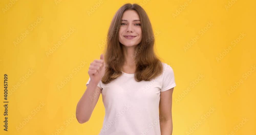 Cheerful confident lady gesturing thumb up, showing like and approval gesture, orange studio background, slow motion
