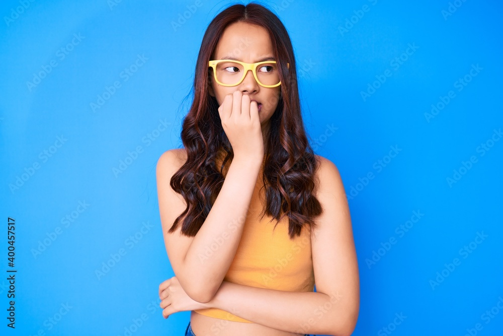 Young beautiful chinese girl wearing casual clothes and glasses looking stressed and nervous with hands on mouth biting nails. anxiety problem.