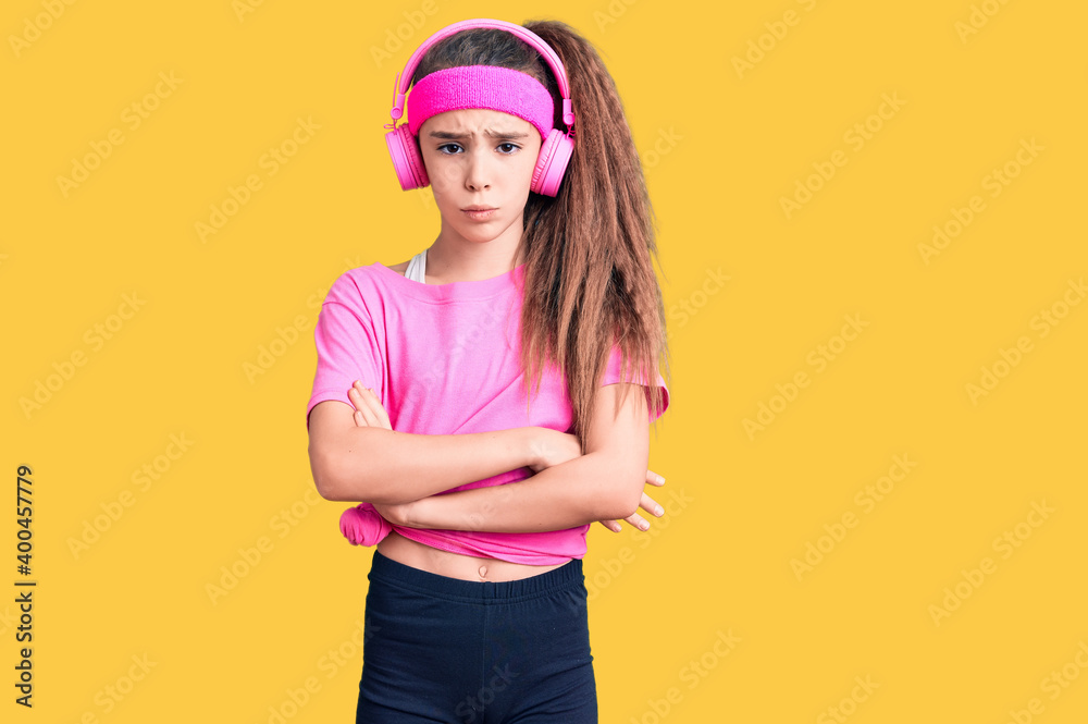 Cute hispanic child girl wearing gym clothes and using headphones skeptic and nervous, disapproving expression on face with crossed arms. negative person. Cute hispanic child girl wearing gym clothes and using headphones skeptic and nervous, disapproving expression on face with crossed arms. negative person.