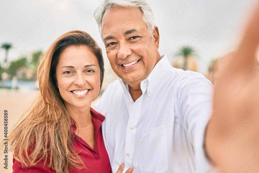 Middle age hispanic couple smiling happy making selfie by the camera at the beach. Middle age hispanic couple smiling happy making selfie by the camera at the beach.