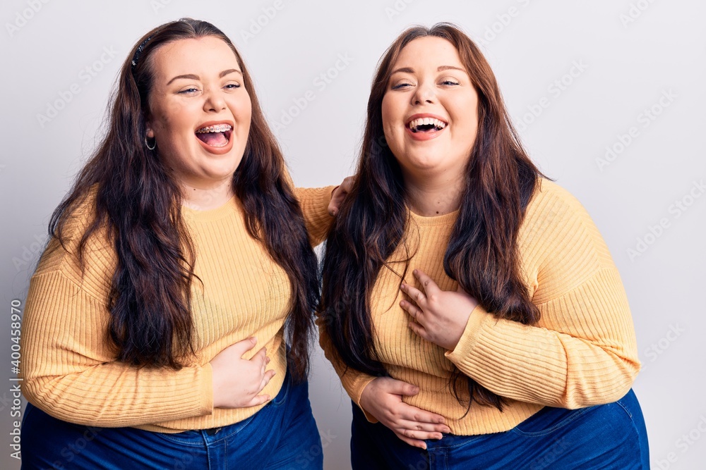 Young plus size twins wearing casual clothes smiling and laughing hard out loud because funny crazy joke with hands on body. Young plus size twins wearing casual clothes smiling and laughing hard out loud because funny crazy joke with hands on body.