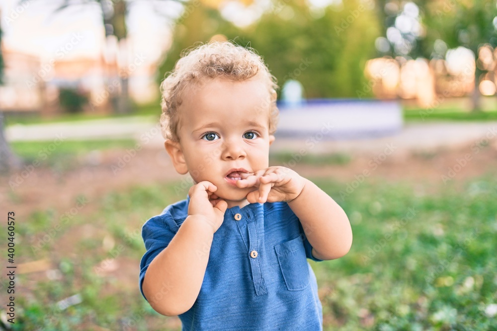 Sad little boy putting fingers on mouth touching gums because toothache at the park on a sunny day. Beautiful blonde hair male toddler in pain for new baby teeth outdoors Sad little boy putting fingers on mouth touching gums because toothache at the park on a sunny day. Beautiful blonde hair male toddler in pain for new baby teeth outdoors