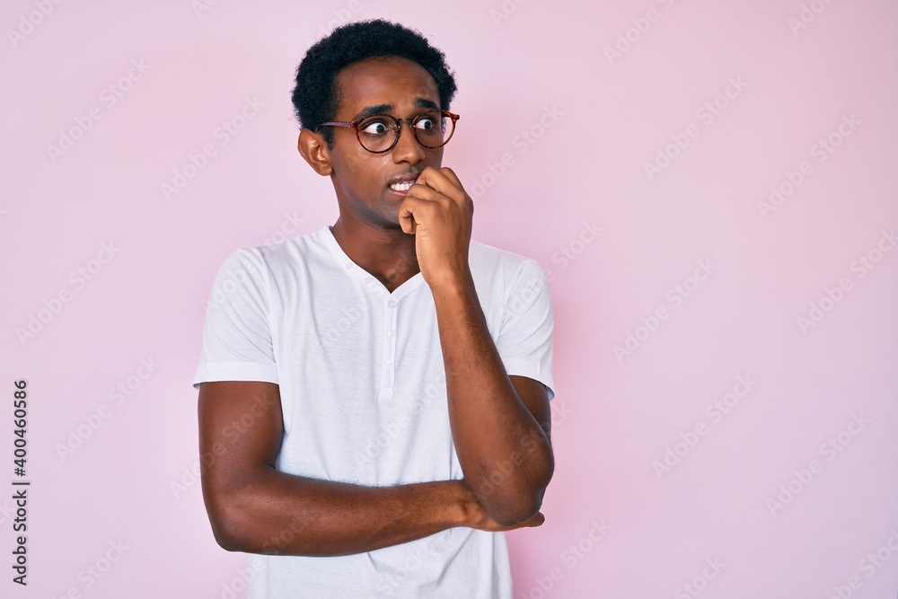 African handsome man wearing casual clothes and glasses looking stressed and nervous with hands on mouth biting nails. anxiety problem. African handsome man wearing casual clothes and glasses looking stressed and nervous with hands on mouth biting nails. anxiety problem.