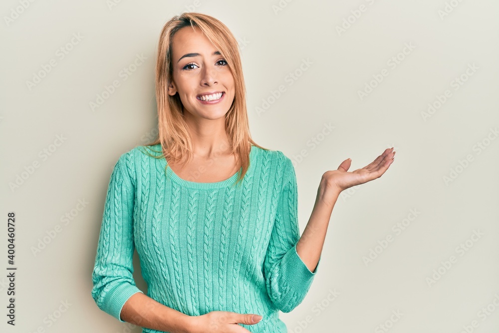 Beautiful blonde woman wearing casual winter sweater smiling cheerful presenting and pointing with palm of hand looking at the camera.
