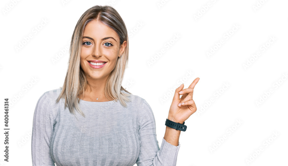 Beautiful blonde woman wearing casual clothes with a big smile on face, pointing with hand finger to the side looking at the camera. Beautiful blonde woman wearing casual clothes with a big smile on face, pointing with hand finger to the side looking at the camera.