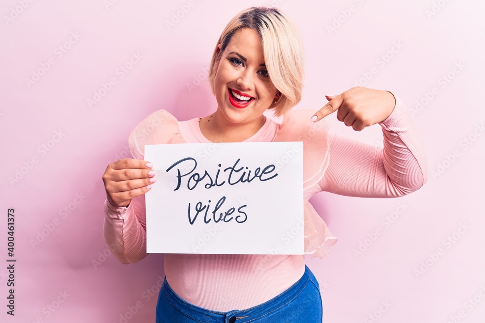 Blonde plus size woman asking for optimist attitude holding paper with positive vibes message smiling happy pointing with hand and finger Blonde plus size woman asking for optimist attitude holding paper with positive vibes message smiling happy pointing with hand and finger