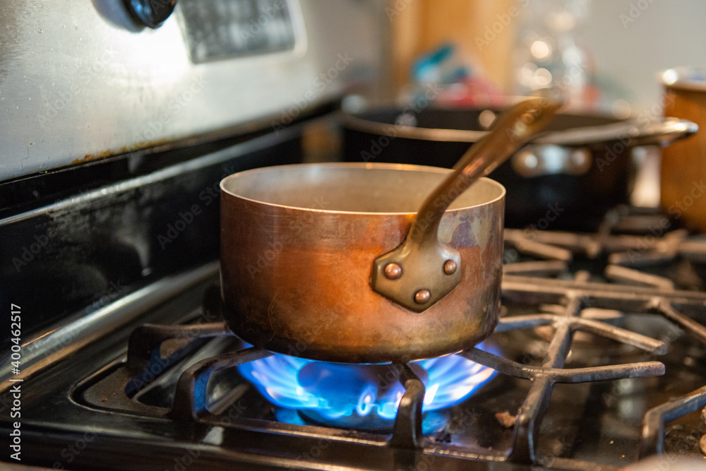 A close up of a worn stainless steel pot with a long metal handle sits