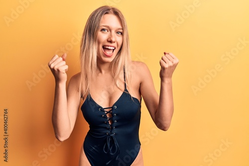 Young beautiful blonde girl wearing swimwear screaming proud, celebrating victory and success very excited with raised arms