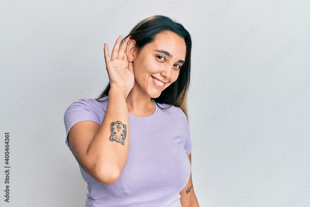 Young hispanic woman wearing casual clothes smiling with hand over ear listening and hearing to rumor or gossip. deafness concept. Young hispanic woman wearing casual clothes smiling with hand over ear listening and hearing to rumor or gossip. deafness concept.