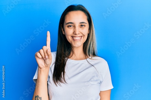Young hispanic woman wearing casual white t shirt showing and pointing up with finger number one while smiling confident and happy.
