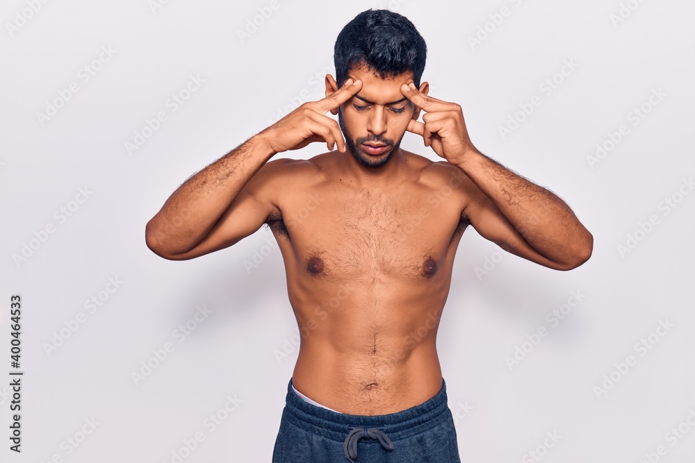 Fototapeta premium Young latin man standing shirtless with hand on head for pain in head because stress. suffering migraine.
