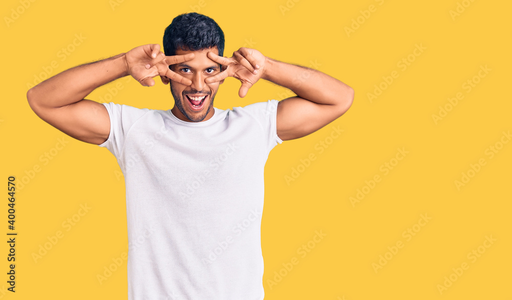 Young latin man wearing casual clothes doing peace symbol with fingers over face, smiling cheerful showing victory Young latin man wearing casual clothes doing peace symbol with fingers over face, smiling cheerful showing victory