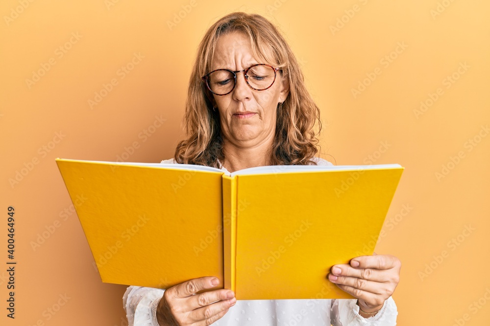 Middle age blonde woman reading a book wearing glasses clueless and confused expression. doubt concept. Middle age blonde woman reading a book wearing glasses clueless and confused expression. doubt concept.