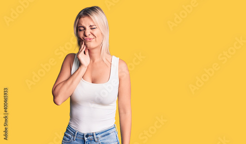 Young beautiful blonde woman wearing casual sleeveless t-shirt touching mouth with hand with painful expression because of toothache or dental illness on teeth. dentist