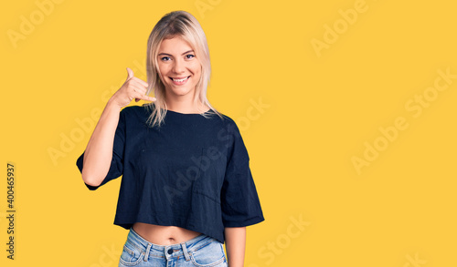 Young beautiful blonde woman wearing casual t-shirt smiling doing phone gesture with hand and fingers like talking on the telephone. communicating concepts.