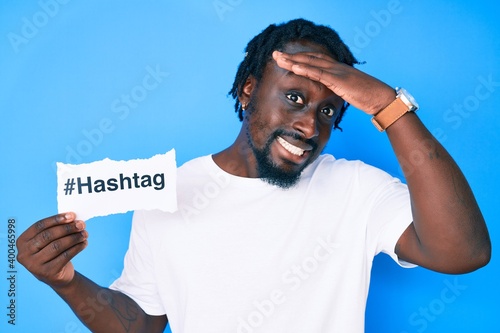 Young african american man with braids holding hashtag paper stressed and frustrated with hand on head, surprised and angry face
