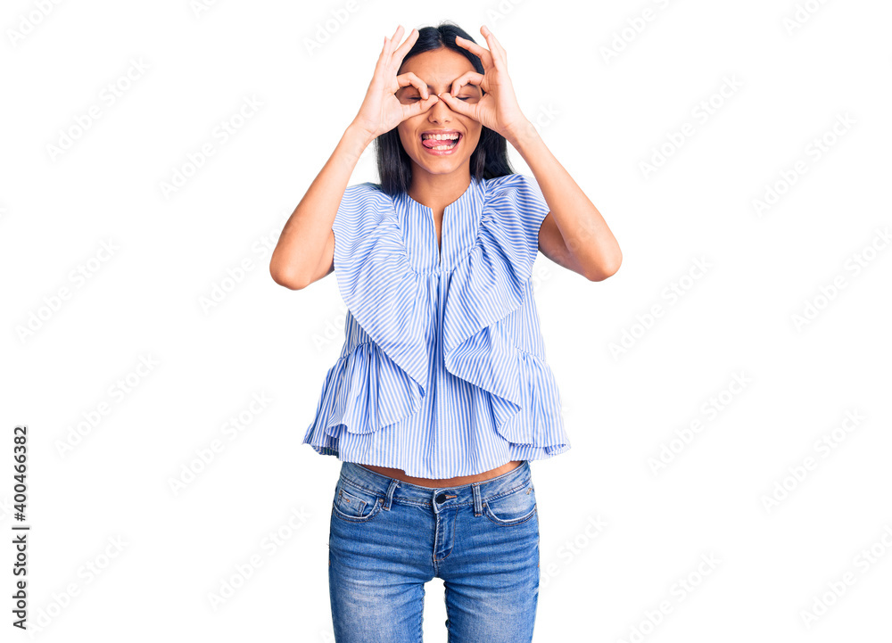 Young beautiful latin girl wearing casual clothes doing ok gesture like binoculars sticking tongue out, eyes looking through fingers. crazy expression. Young beautiful latin girl wearing casual clothes doing ok gesture like binoculars sticking tongue out, eyes looking through fingers. crazy expression.