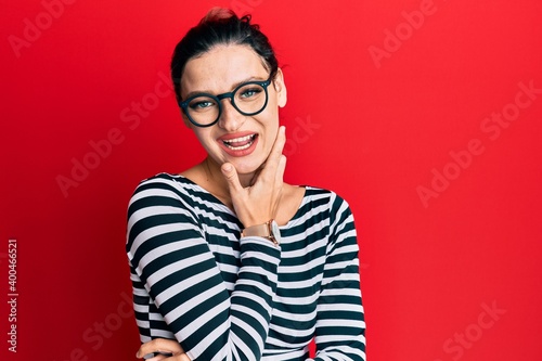 Young caucasian woman wearing casual clothes and glasses looking confident at the camera smiling with crossed arms and hand raised on chin. thinking positive.