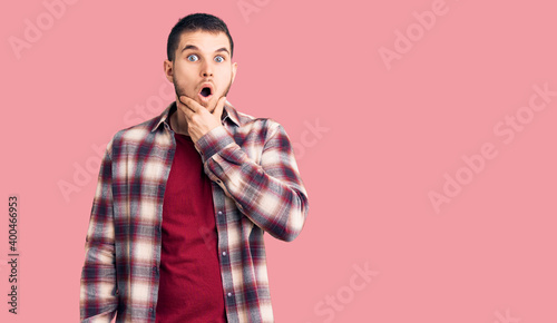 Young handsome man wearing casual shirt looking fascinated with disbelief  surprise and amazed expression with hands on chin