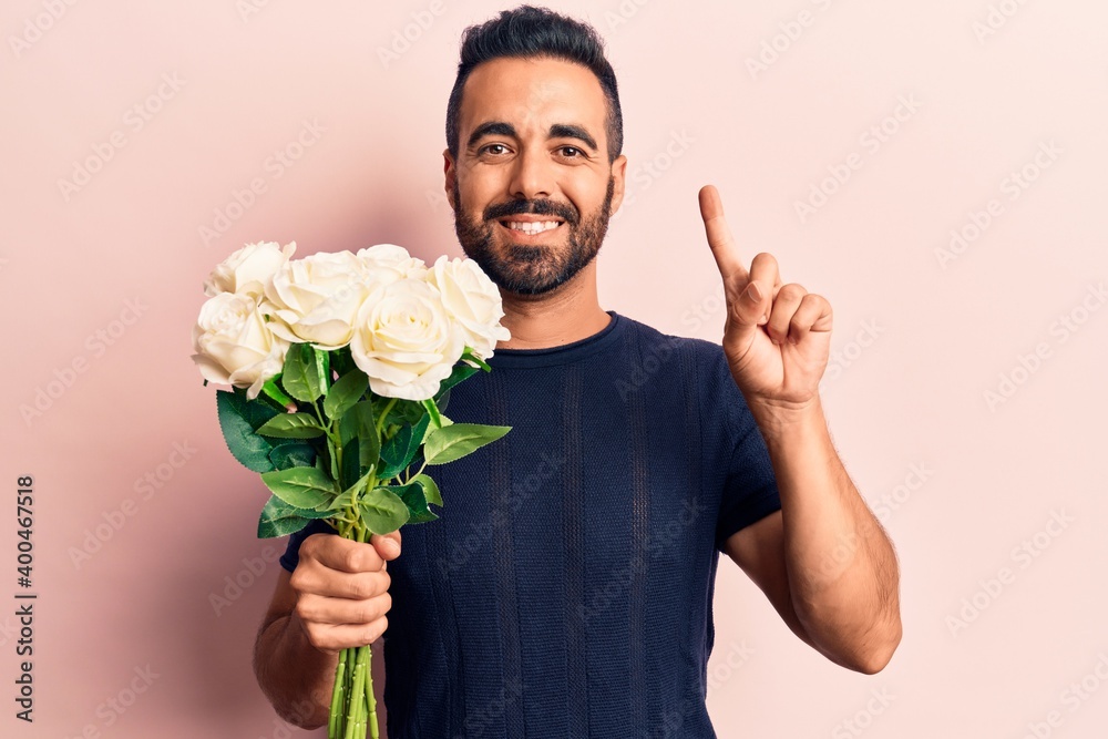 Young hispanic man holding flowers smiling with an idea or question pointing finger with happy face, number one Young hispanic man holding flowers smiling with an idea or question pointing finger with happy face, number one