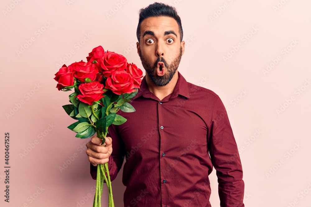 Young hispanic man holding flowers scared and amazed with open mouth for surprise, disbelief face Young hispanic man holding flowers scared and amazed with open mouth for surprise, disbelief face
