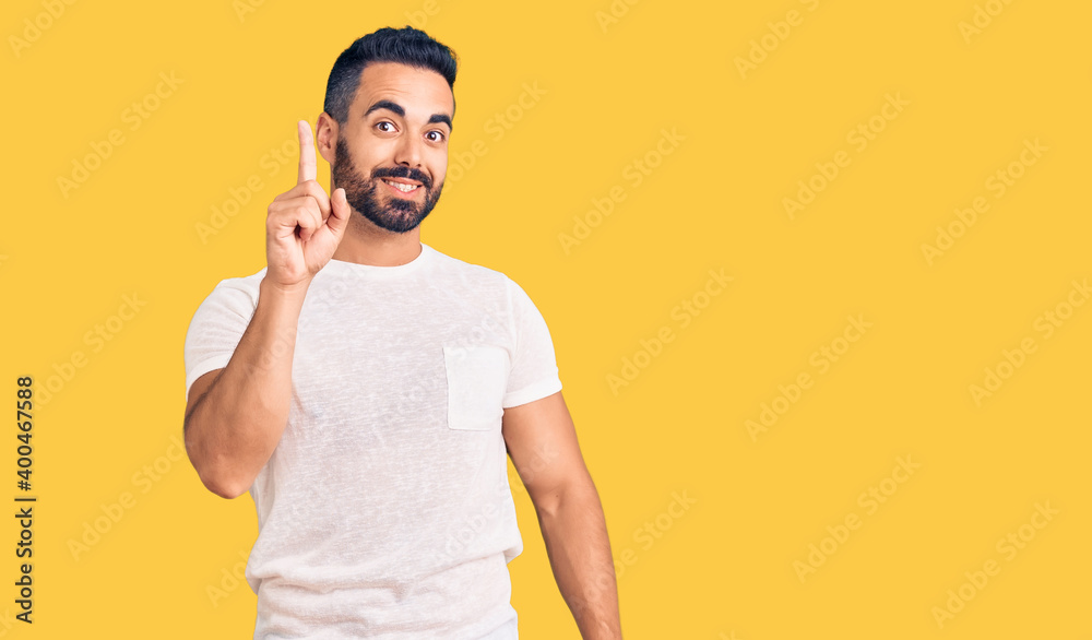 Young hispanic man wearing casual clothes showing and pointing up with finger number one while smiling confident and happy. Young hispanic man wearing casual clothes showing and pointing up with finger number one while smiling confident and happy.