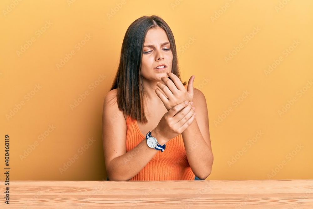 Young caucasian woman wearing casual clothes sitting on the table suffering pain on hands and fingers, arthritis inflammation Young caucasian woman wearing casual clothes sitting on the table suffering pain on hands and fingers, arthritis inflammation