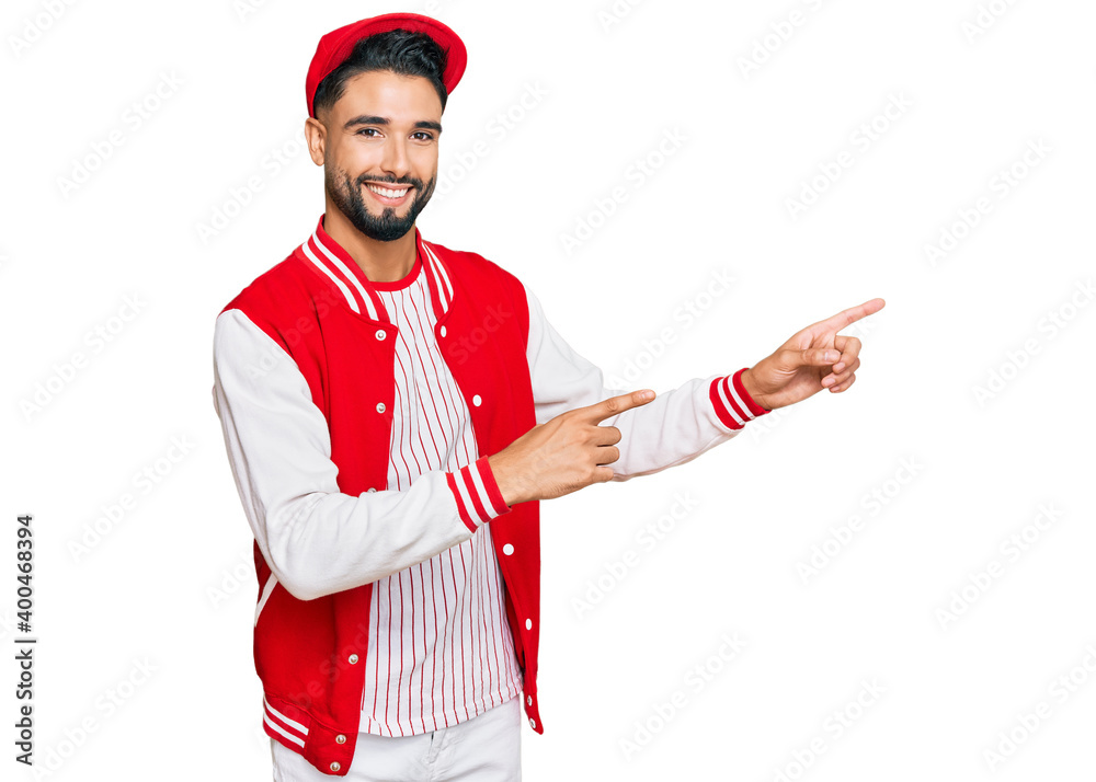 Young man with beard wearing baseball uniform smiling and looking at the camera pointing with two hands and fingers to the side. Young man with beard wearing baseball uniform smiling and looking at the camera pointing with two hands and fingers to the side.