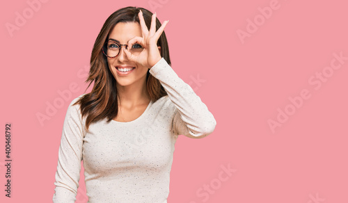 Young brunette woman wearing casual clothes and glasses doing ok gesture with hand smiling, eye looking through fingers with happy face.