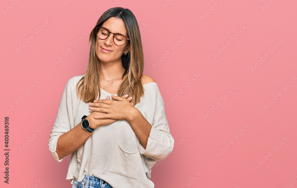 Young woman wearing casual clothes and glasses smiling with hands on chest with closed eyes and grateful gesture on face. health concept.