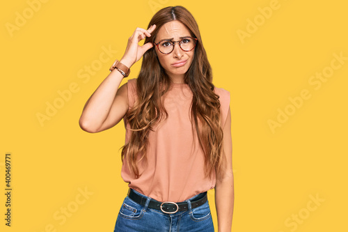 Young hispanic woman wearing casual clothes and glasses worried and stressed about a problem with hand on forehead, nervous and anxious for crisis