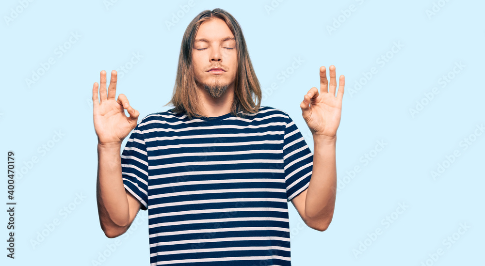 Handsome caucasian man with long hair wearing casual striped t-shirt relax and smiling with eyes closed doing meditation gesture with fingers. yoga concept. Handsome caucasian man with long hair wearing casual striped t-shirt relax and smiling with eyes closed doing meditation gesture with fingers. yoga concept.