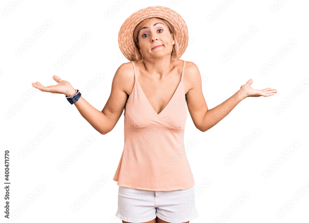 Young blonde woman wearing summer hat clueless and confused expression with arms and hands raised. doubt concept. Young blonde woman wearing summer hat clueless and confused expression with arms and hands raised. doubt concept.
