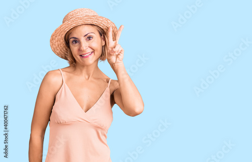 Young blonde woman wearing summer hat showing and pointing up with fingers number two while smiling confident and happy. © Krakenimages.com