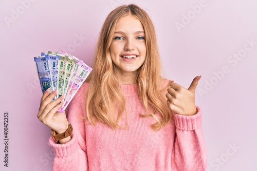 Beautiful young caucasian girl holding indian rupee banknotes smiling happy and positive, thumb up doing excellent and approval sign