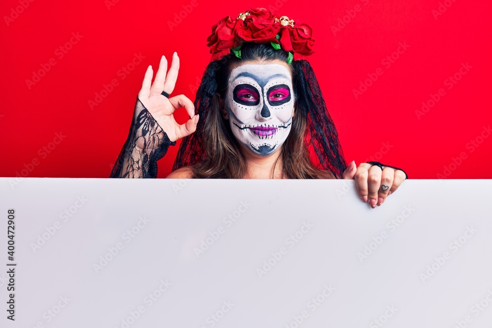Young woman wearing day of the dead costume holding blank empty banner doing ok sign with fingers, smiling friendly gesturing excellent symbol