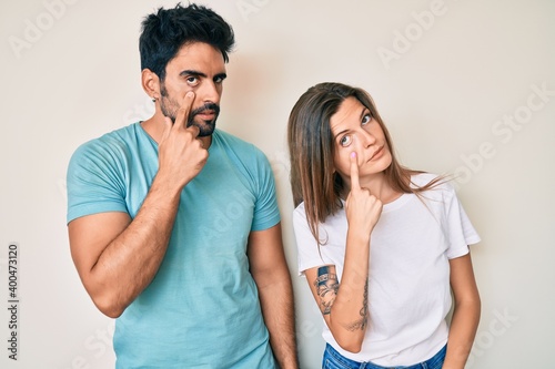 Beautiful young couple of boyfriend and girlfriend together pointing to the eye watching you gesture, suspicious expression