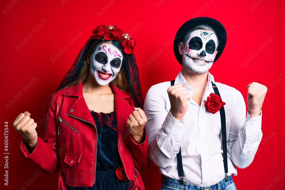 Couple wearing day of the dead costume over red very happy and excited doing winner gesture with arms raised, smiling and screaming for success. celebration concept. Couple wearing day of the dead costume over red very happy and excited doing winner gesture with arms raised, smiling and screaming for success. celebration concept.