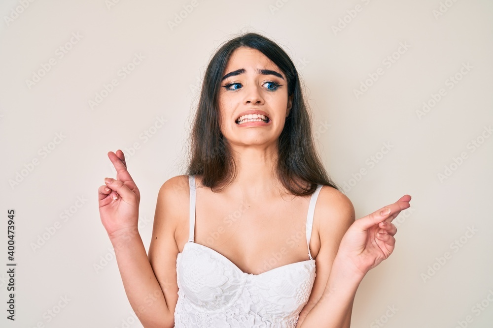 Brunette teenager girl posing elegant gesturing finger crossed smiling with hope and eyes closed. luck and superstitious concept. Brunette teenager girl posing elegant gesturing finger crossed smiling with hope and eyes closed. luck and superstitious concept.