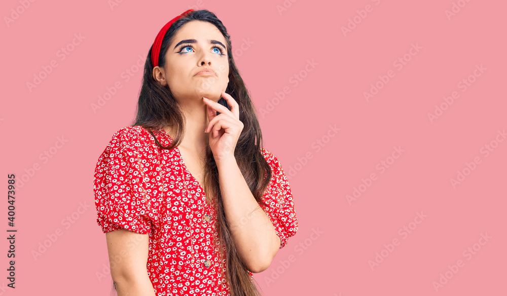 Fototapeta premium Brunette teenager girl wearing summer dress with hand on chin thinking about question, pensive expression. smiling and thoughtful face. doubt concept.