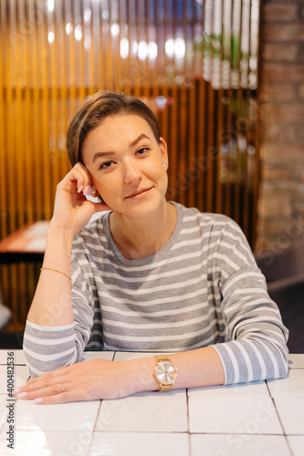 Cute portrait of a young woman with short hair in a cafe, she's sitting with her hand touching her chin photo