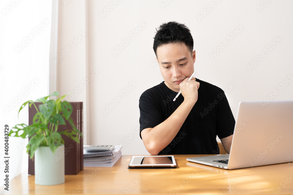 Asian young man in black shirt working on laptop computer and tablet at home Asian young man in black shirt working on laptop computer and tablet at home