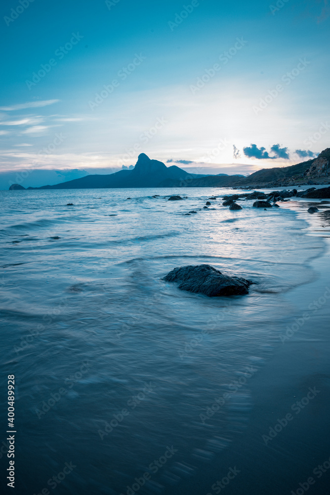 Sunset or sunrise in ocean, nature landscape background, pink clouds flying in sky to shining sun above sea with rocks sticking up of water surface