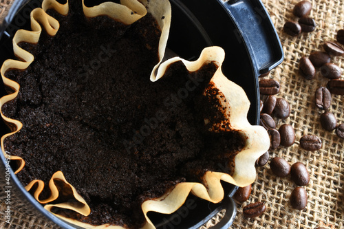An image of a used coffee filter with coffee basket and coffee beans on burlap.