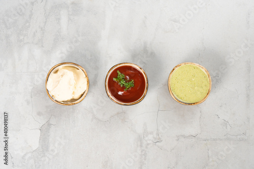 A set of three sauces in small round saucers on a light neutral concrete table. Ketchup, mayonnaise cheese sauce and garlic sauce with herbs.