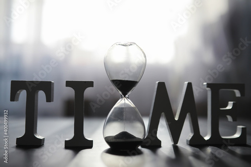 The concept of the passage of time. Hourglass on a dark background. Inscription time. The shadow on the surface of the word.